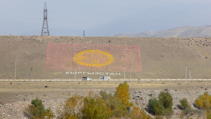 the flag of Kyrgyzstan on the hill with the highway of countryside, one belt one way transport...