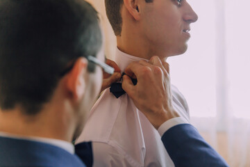 A man is getting his tie tied by another man. The man getting his tie tied is wearing a blue suit and a white shirt