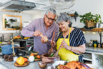 Latin senior couple cooking a turkey meat together for Christmas dinner at home in Mexico Latin...