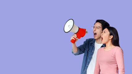 Angry asian couple shouting together towards copy space through megaphone, grey background, panorama
