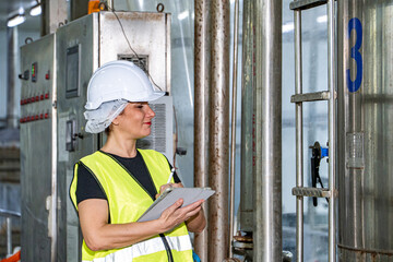 Female industrial engineer wearing a white helmet while standing in a heavy industrial factory