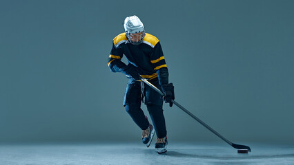 Man, ice hockey athlete in black and yellow uniform during powerful game on ice, captured in athletic stance against studio background. Concept of sport, game, tournament, action, competition