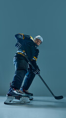 Fototapeta premium Vertical full-length image of concentrated man, hockey player in helmet and uniform, standing with stick, preparing for intensive game. Concept of sport, game, tournament, action, competition