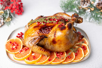 Chicken baked whole to appetizing crispy crust with pomegranate and red orange. Traditional New Year and Christmas dish. In the background are Christmas decorations. Close-up, selective focus.