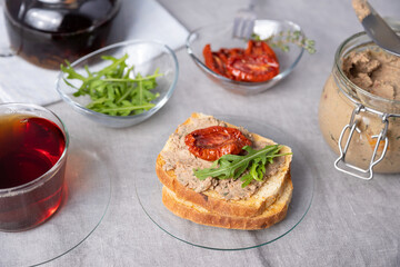 Chicken liver pate with wheat bread, arugula, sun-dried tomatoes and black tea. Homemade traditional rustic cuisine. Breakfast or snack option. Selective focus, close-up.