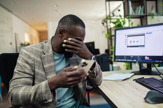 Stressed man in office holding phone and covering face