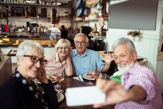 Group of happy senior friends taking selfie together in restaurant - Powered by Adobe
