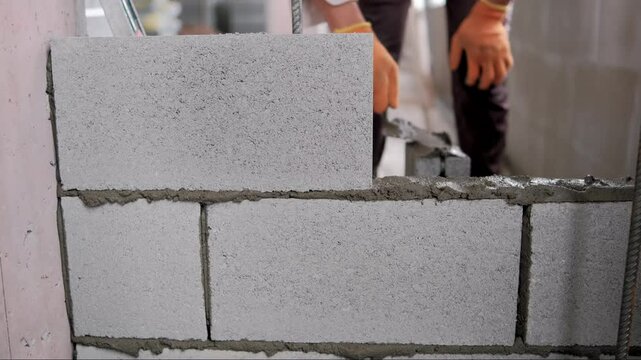 Construction worker is carefully laying concrete blocks, applying mortar and positioning each block with precision