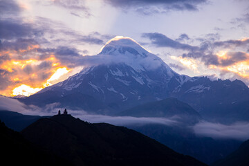 Majestic Mount Kazbek in Georgia illuminated by the last rays of a fleeting sunset, breaking...