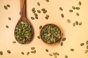 Fresh pumpkin seeds in wooden bowl and in spoon on beige background, top view flat lay. Organic eco healthy seeds, superfood, diet food, healthy vegetarian food. Smoothie Ingredient 