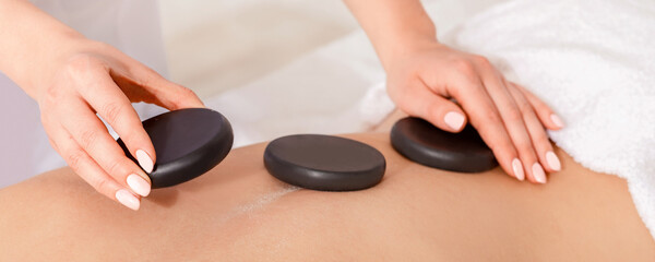 Spa treatments for beauty. Female hands lay hot stones on woman backs on massage table, close up,...