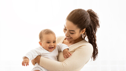 Mom's Son. Joyful Black Mommy Carrying Little Baby In Arms Cuddling And Playing With Cute Infant Standing Near Window At Home. Joy Of Motherhood, Maternity Leave And Child Care