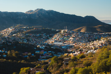 Obraz premium A scenic view of Guanajuato, Mexico and its colourful sprawl nestled among rolling hills and rugged mountains, showcasing its vibrant urban landscape and natural backdrop.
