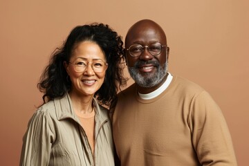 Fototapeta premium Portrait of a merry multicultural couple in their 40s showing off a lightweight base layer over pastel brown background