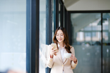 Businesswoman smiling while holding a coffee cup and checking her phone during a work break