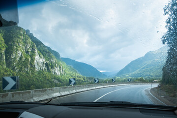 A wet road on a cloudy and rainy day seen from inside a vehicle. There is a sharp curve well signposted. Concept of driving, transportation and caution on the road © LaMorenita