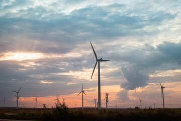 Obraz premium side view of a large wind farm with a nice stormy sky at sunset. The windmills or generators face the sun and the sky is full of clouds