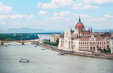 Fototapeta premium Tour-boats traveling on the Danube River pass the Hungarian Parliament Building, with the Margaret Bridge in the background, on a sunny, summer day.