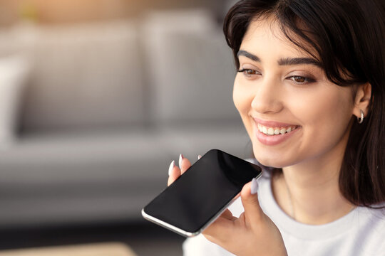 Closeup portrait of smiling young woman holding cellphone near mouth using mobile voice recognition or digital assistance app speaking with virtual assistant, recording message talking on smartphone
