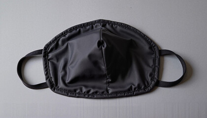 Dark grey face mask laid flat on a grey surface with copy space