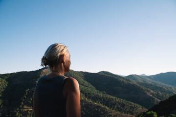 Naklejka premium A woman gazes at a lush, green mountain landscape under a bright blue sky, showing appreciation for the beauty of nature