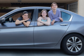 Three Females Looking at Camera While Seated in Sedan Parked Outside, Near Sundown, horizontal