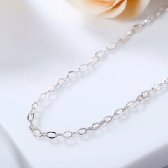 A delicate silver chain necklace elegantly displayed with a soft rose in the background.