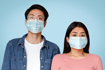 Coronavirus Concept. Frightened asian couple posing in protective medical face masks, standing over light background in studio, empty space