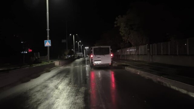 This video shows a white van driving on a wet road at night, with a following car keeping a close distance.