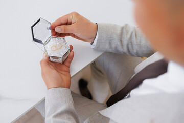 A man is holding a small box with a ring inside. The box is silver and has a hexagonal shape. The...