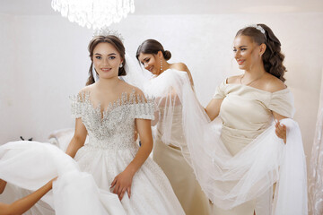 A bride is getting ready for her wedding with her bridesmaids. The bride is wearing a beautiful white dress with a tiara on her head. The bridesmaids are helping her get ready