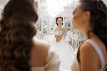 A woman in a wedding dress is standing in front of two other women. The women are smiling and looking at the bride