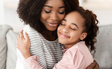 Family Love And Tenderness. Closeup portrait of happy black woman with curly hair embracing cute little girl with closed eyes, spending free time together. Smiling mother and daughter hugging at home