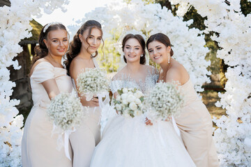 A bride and her bridesmaids pose for a picture in front of a white arch. The bride is wearing a...