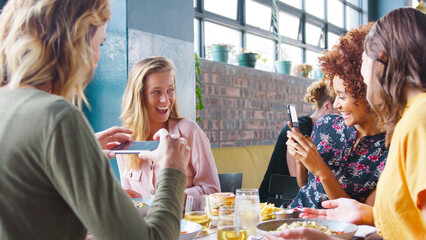 Group Of Young Female Friends Taking Photos Of Food In Restaurant To Post On Social Media
