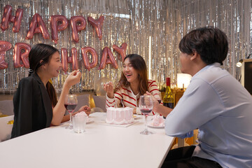 Happy friends with tasty cake and glasses of sparkling wine celebrating birthday indoors