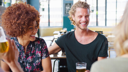 Group Of Young Smiling Friends Sitting At Table Meeting For Drinks In Bar 