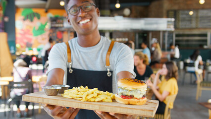 Close Up Of Male Server With Burger And Fries In Busy Bar Restaurant 