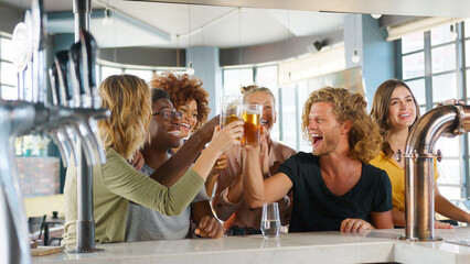 Group Of Young Male And Female Friends Celebrating Whilst Watching Game On Screen In Sports Bar