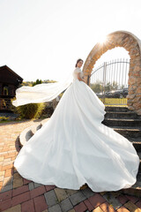 Fototapeta premium A woman in a white dress is posing in front of a stone archway. The dress is long and flowing, and the woman is wearing a tiara. Concept of elegance and sophistication, as the woman's attire