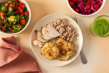 A healthy meal of green buckwheat with chicken breast, zucchini pancakes, fresh and fermented vegetable salads and celery cucumber smoothie