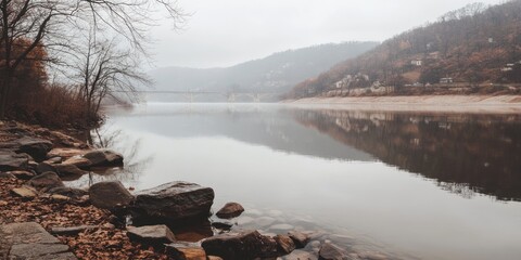 A tranquil river scene with foggy hills and rocky shoreline.