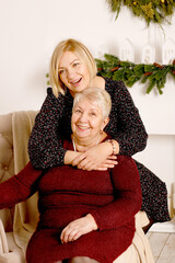 happy daughter hugging mother sitting in armchair near Christmas decorated fireplace