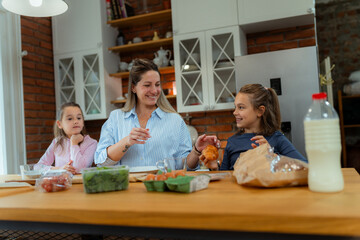 Morning breakfast preparation as mother and daughters gather around counter, working together amid fresh produce and kitchen supplies