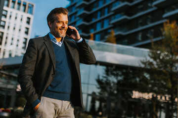 Businessman in smart attire walking while talking on phone in modern urban setting during sunny afternoon