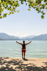 Man with arms in cross in front of an alpine lake with mountains in the background