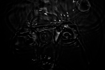 Water droplets hit the black water surface and create waves.
