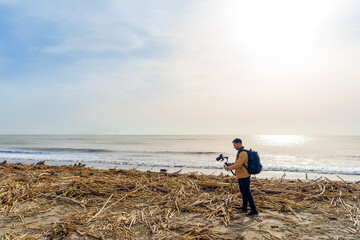 Camera Operator Filming Flood-Damaged Vegetation and Debris Washed Ashore on a Beach Using a Gimbal