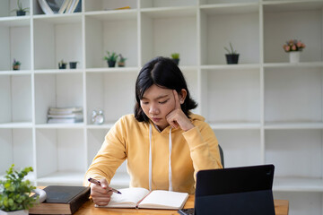 Intelligent young woman having online lessons on laptop, drinking coffee and taking notes,