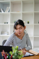 Intelligent young woman having online lessons on laptop, drinking coffee and taking notes,